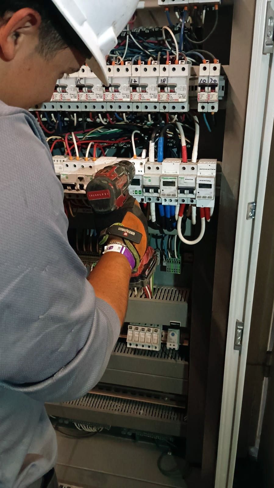 Técnico con casco trabajando en un tablero eléctrico con protecciones y medidores