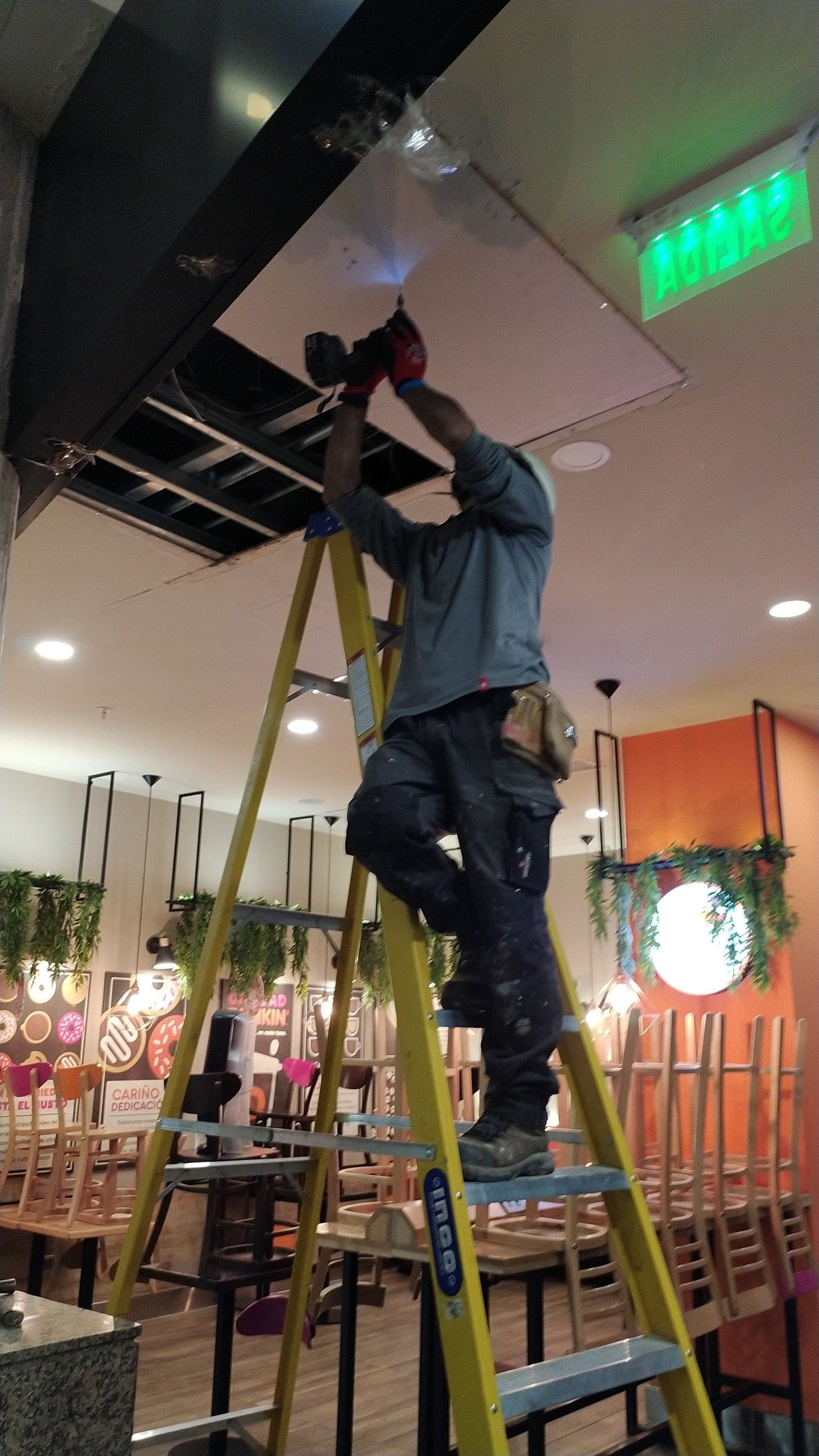 Técnico sobre escalera reparando el cielo de un local comercial
