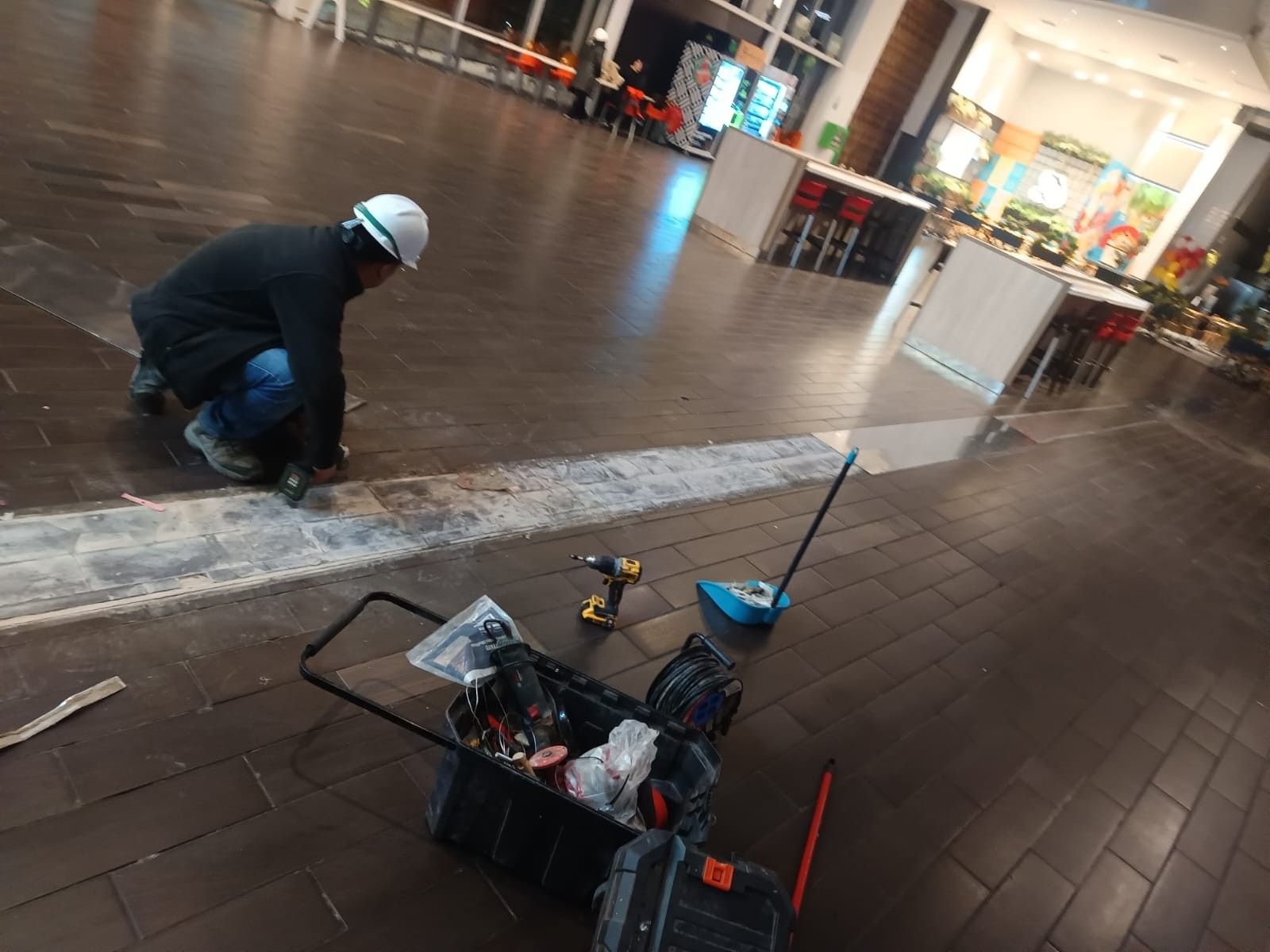 Técnico con casco interviniendo una junta de piso en un patio de comidas